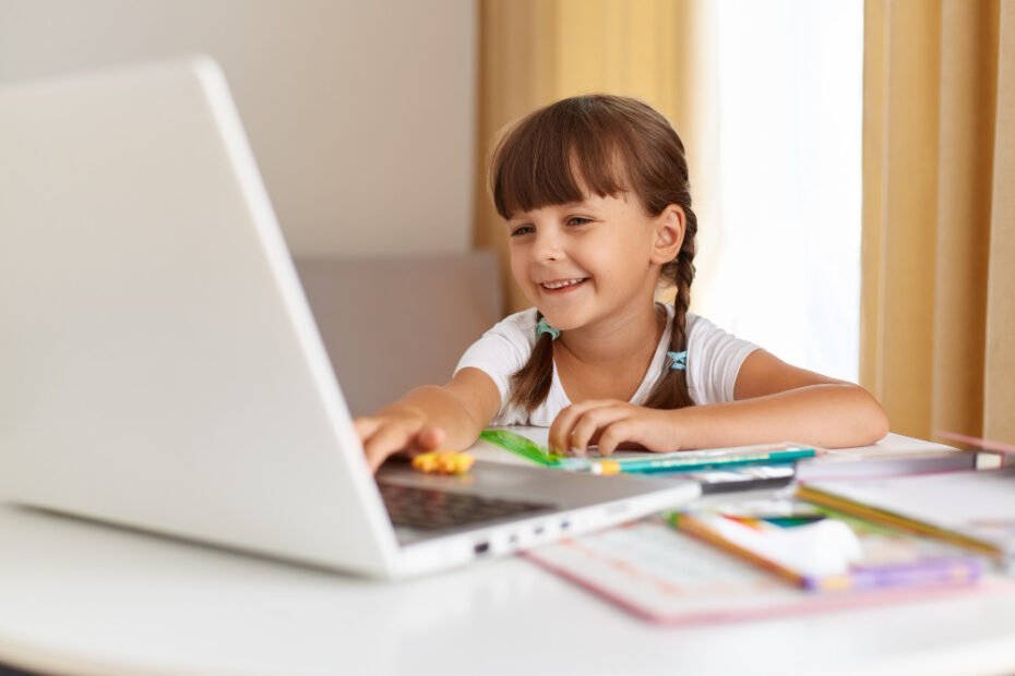 Criança sorrindo em frente ao computador com alguns livros na mesa