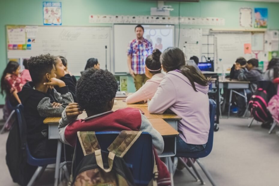 Alunos reunidos em uma mesa com o professor e a lousa ao fundo.